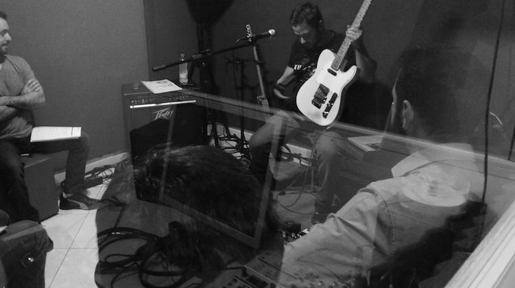 Denis Delphin gravando em estúdio, com fone de ouvido, guitarra, amplificador e pedais