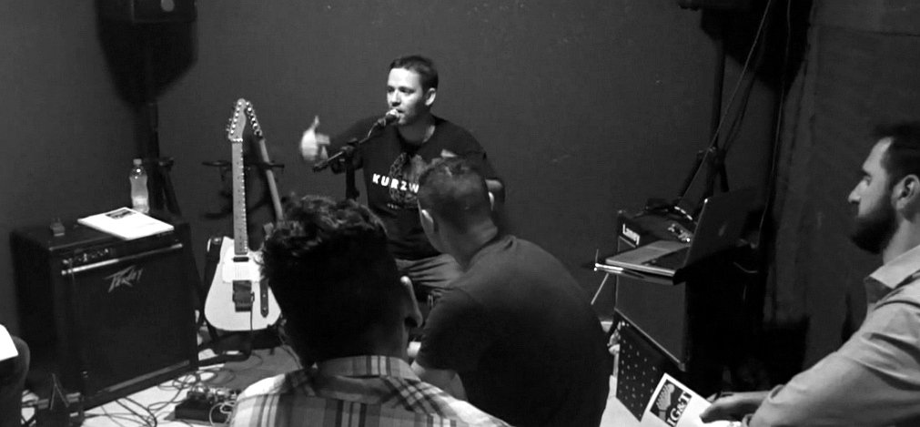 Denis Delphin em palestra, falando ao microfone para o público